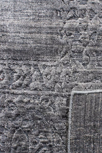 Close-up of a gray patterned rug with a textured, low-pile surface and a visible woven backing along the corner.