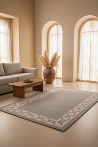 A large rectangular area rug with a gray center and a beige chain-link border, styled in a warm, modern living room with a sofa, wooden coffee table, and arched windows.