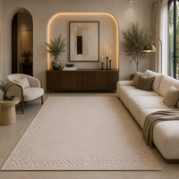 A large rectangular area rug in a warm cream or light beige tone with a textured geometric border, styled in a modern, elegant living room with a cream sofa, wooden console, and warm ambient lighting.